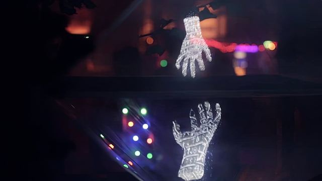 Two projected hands reach towards one another across a dark reflective surface.