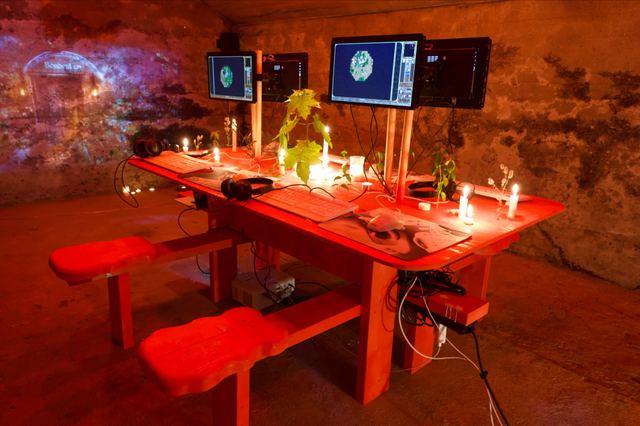 The empty cellar glows orange around a handmade red gaming table, with four seats, back-to-back screens, candles and a projection on the stone wall.