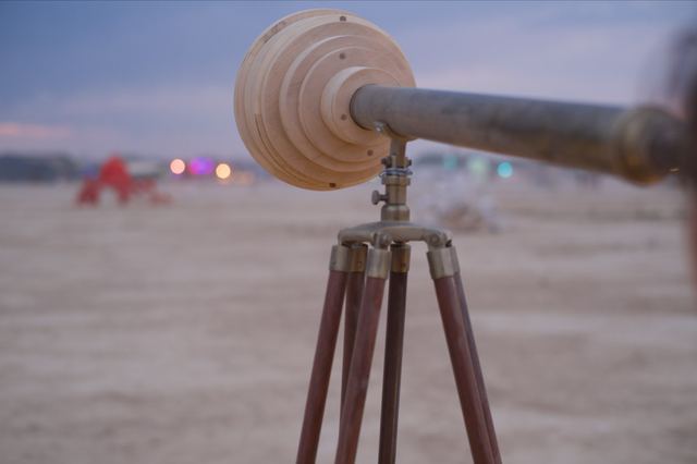 A close view of the telescope's stepped wooden housing, brass tube and tripod, with coloured lights out of focus across the desert.