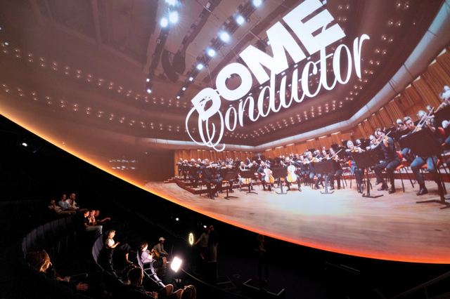 The Dome Conductor title and an orchestra fill the curved projection above a seated audience at Wisdome Stockholm.