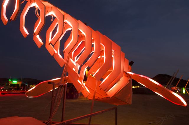 A close view along the illuminated ribs towards the whale's head, showing red LED tubes, cables and the spread fins.
