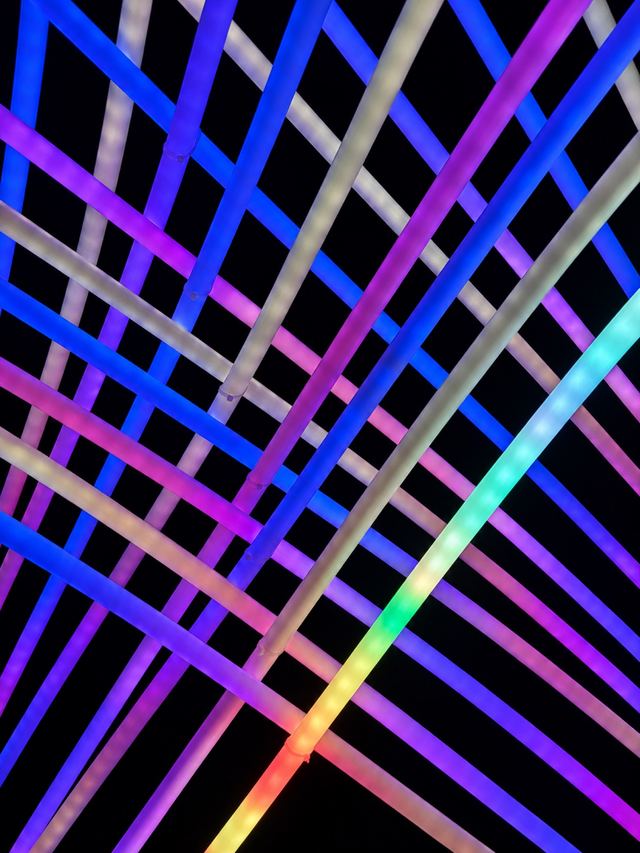 A close view of diagonal tubes crossing in a dense weave of pink, violet, blue and green light against the dark.