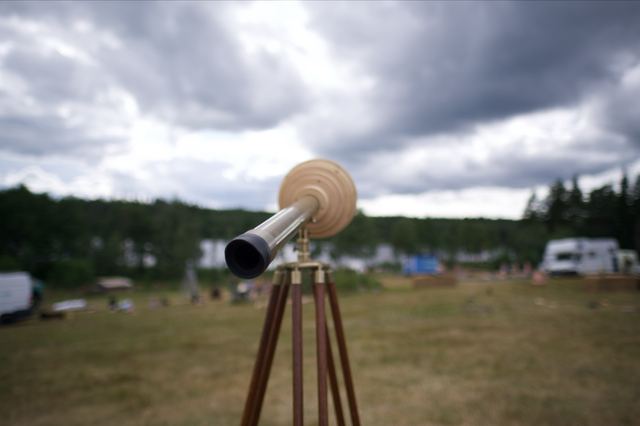 A close view along the brass telescope towards its eyepiece, with grass and trees behind it.