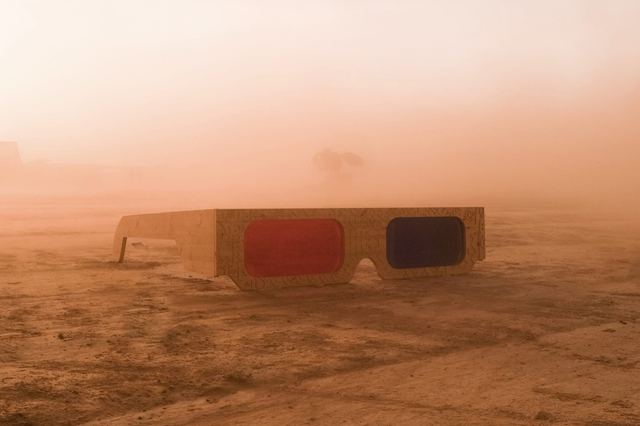 An oversized pair of red-and-blue 3D glasses rests on a dusty plain in warm evening light.