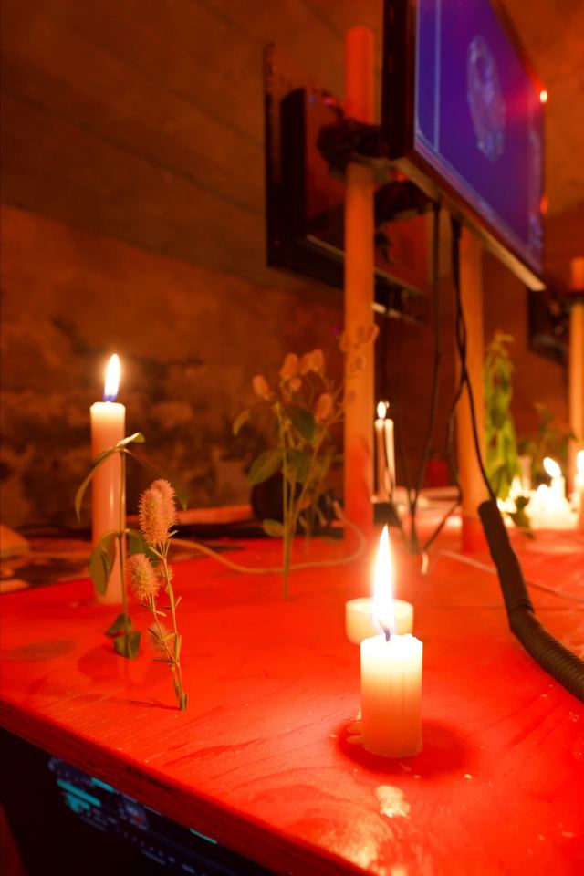 Candles and stems of grass sit between the wooden monitor supports on the red tabletop.