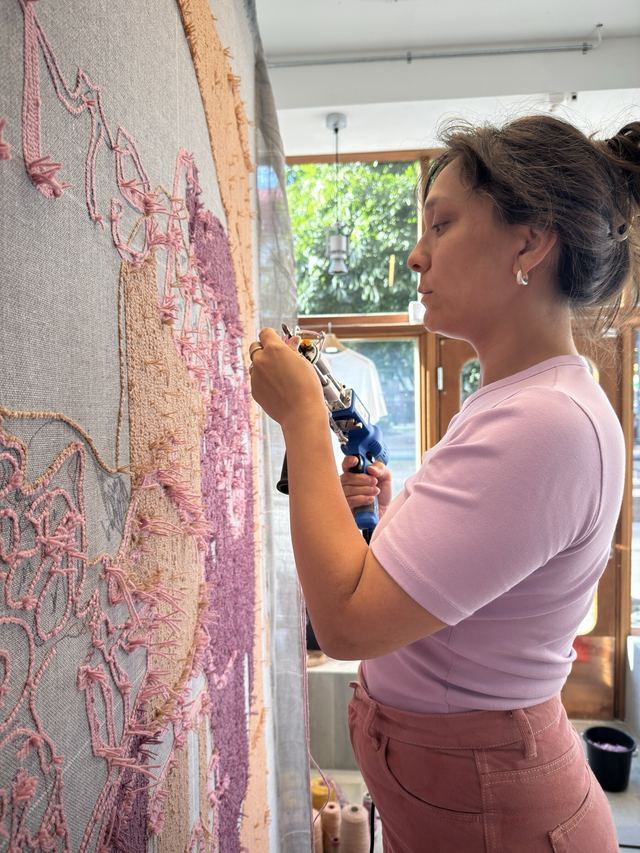 Rose guides a blue tufting gun through the cloth, following the pink yarn outlines.