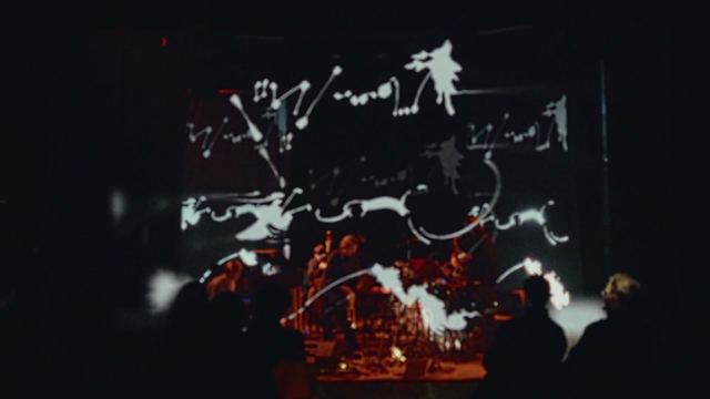 Forty-five seconds from the performance: the quintet plays while a graphic score is drawn live across the projection behind them.
