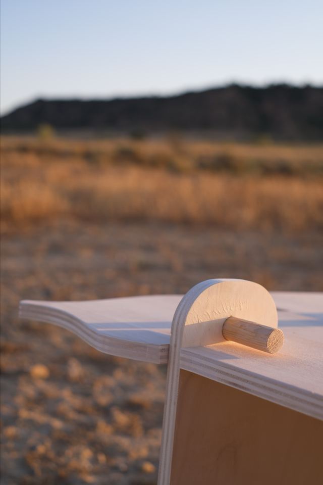A close view of the bench's plywood seat and rounded upright, secured with a wooden peg.