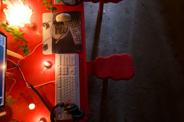 A gaming station seen from directly above: white keyboard and mouse, headphones, candlelight and the red wooden seat beside the table.