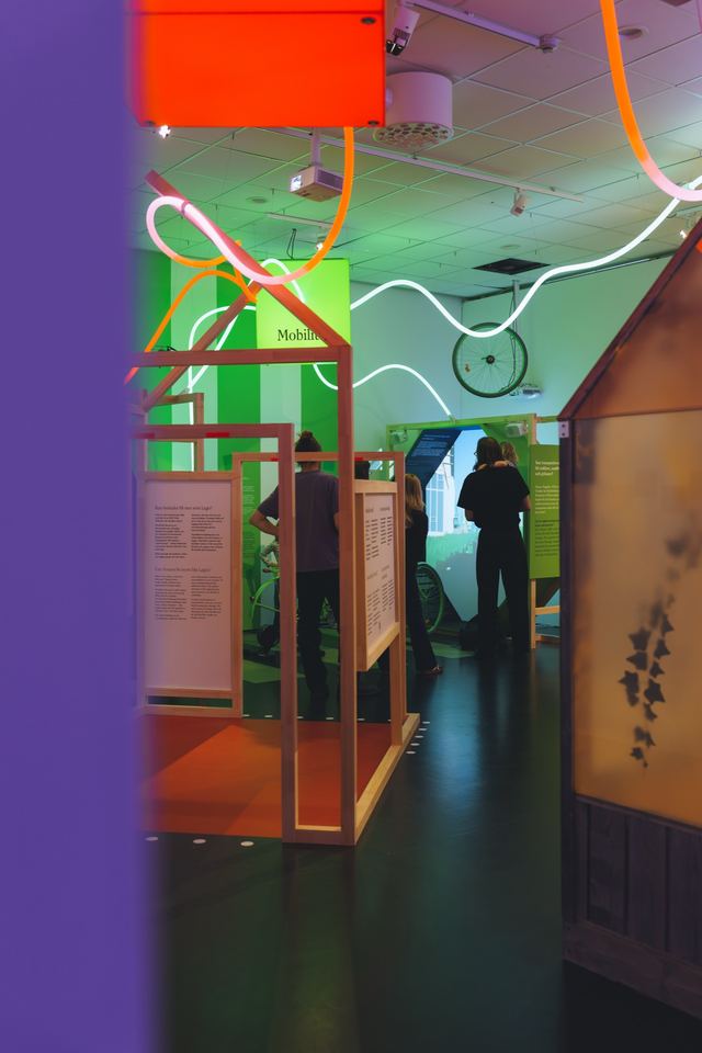 Glowing white lines loop above a narrow passage between an orange display frame and translucent panels.