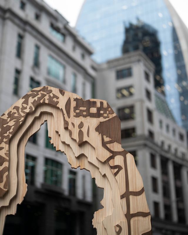 A carved wooden arch frames the surrounding London buildings, bringing an ornamental doorway into the street.