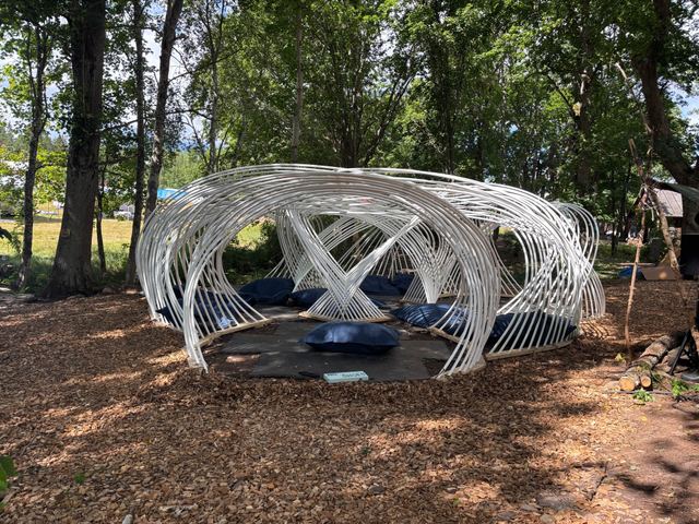 Kagora in daylight: white arches surround a floor of dark mats and blue cushions in the woodland.