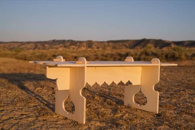 Rose Hallgren's wooden bench stands in the desert in warm evening light, with curved cutouts in its legs and a scalloped edge beneath the seat.