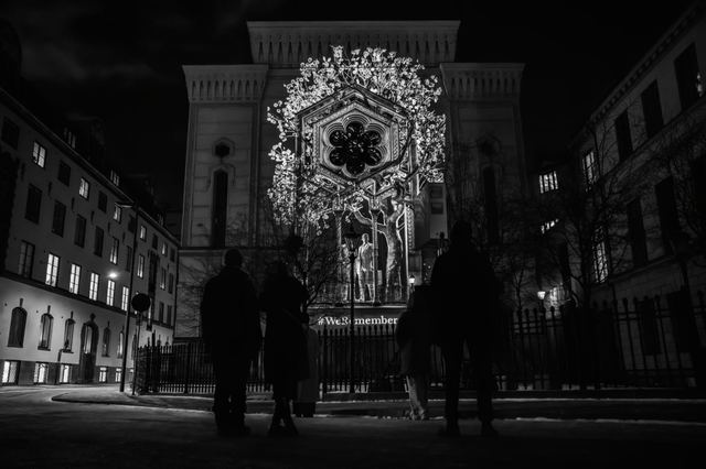 A monochrome projection of sculpted figures covers the Great Synagogue as visitors watch from the street.