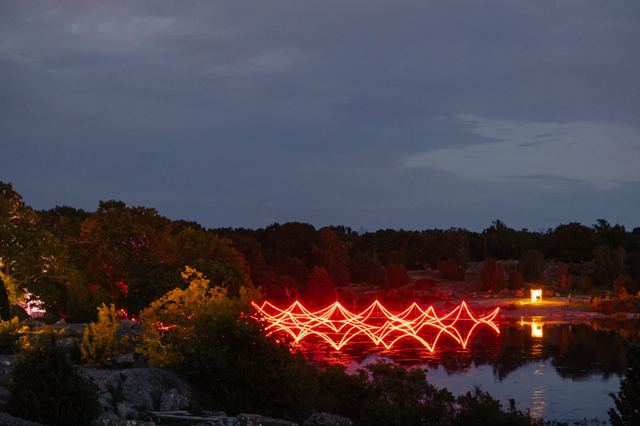 Red arcs of light zigzag along the shoreline at dusk, doubled in the still water below.