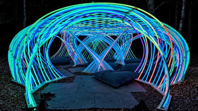 Looking through Kagora's entrance, turquoise and blue arches overlap above empty blue cushions, with pink light deeper inside.