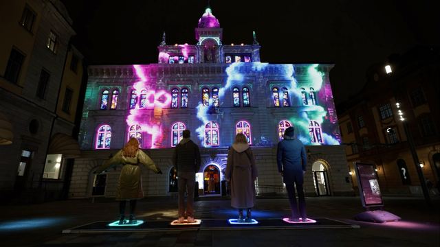 Purple, blue and green projections cover Uppsala Town Hall while people gather around a controller in the square.