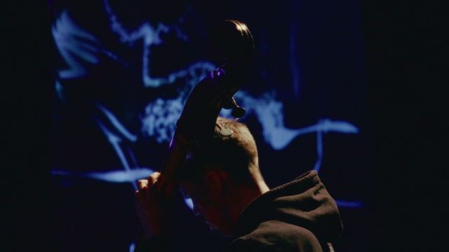 The double bass player seen from behind, the scroll of the bass against a wall of projected white marks.